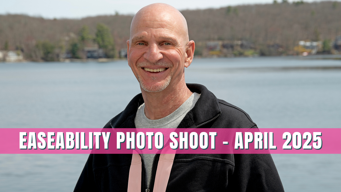 A bald white man - Founder Joey Corasio - smiles in front of a lake wearing a black sweatshirt with pink straps on it. The words "Easeability Photo Shoot - April 2025" are superimposed on the photo in white lettering with a bright pink background. 